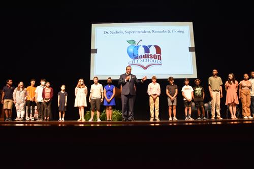 Dr. Nichols with about two dozen kids behind him on stage